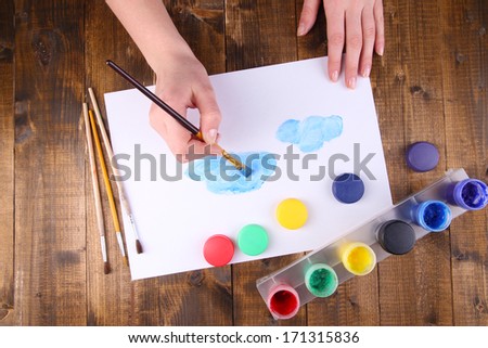 Hand holding brush with paints and paper on wooden background