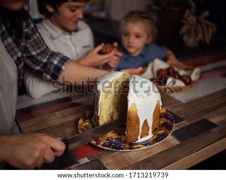 close-up. man cuts Easter cake with raisins covered with white glaze. Easter cake lies on a plate. boy and girl are looking at Easter cake. Image with selective focus. edge vignetting and toning