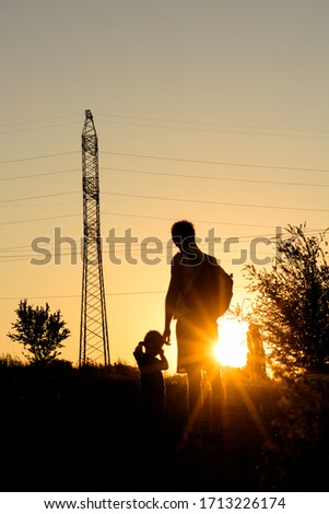 Silhouettes of father and sun standing at the sunset if front of a pylon