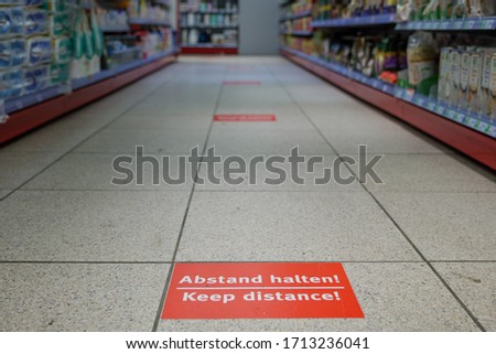Selected focus low angle view at " Abstand halten " means "keep distance", on red rectangular caution sign on the floor inside supermarket in Germany during social distancing by epidemic of COVID-19.