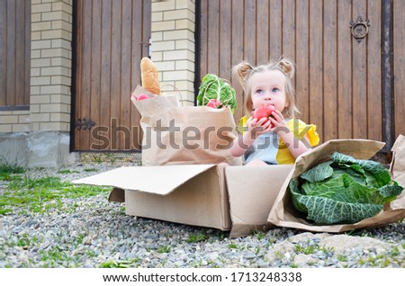 the baby is sitting in a box for delivery. courier delivery of products without contact.
  safe food delivery. contactless delivery near the door. girl eating a tomato in a box. green food