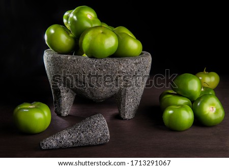 A bunch of Tomatillos or husk tomato in a molcajete in dark food photography in a black background on a wooden rustic table. Concept of Mexican food ingredients to make spicy salsa verde. Still life