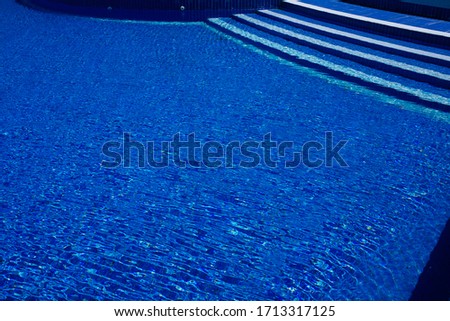 Steps to the pool, blue clear water in the outdoor swimming pool, safe descent, close-up steps through the water. White steps on a blue background, good shape, visibility. Ripples. Copy place