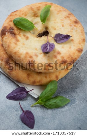 Two ossetian pies with meat on top of each other, vertical shot on a light-blue stone background