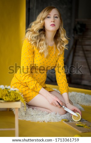 the woman in yellow dress on an yellow background serving lemon 