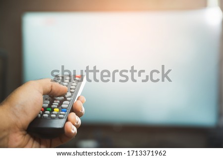 Young man holding television remote control. Hands pointing to tv screen set and turning it on or off select channel watching tv on his sofa at home in the living room relax.