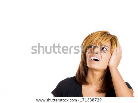 Closeup portrait of a young unhappy stressed woman covering her ears looking up away, to say, stop making that loud noise it's giving me a headache, isolated on white background copy space to left