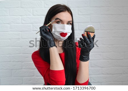 Home beauty industry because of the coronavirus pandemic. A young beautiful girl in a protective mask and gloves stays at home and is engaged in beauty procedures. Girl makes eyebrows and red lips