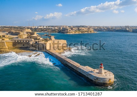Aerial top view of red lighthouse and Fort Ricasoli East Breakwater. Big stormy waves, Mediterranean sea. Malta country