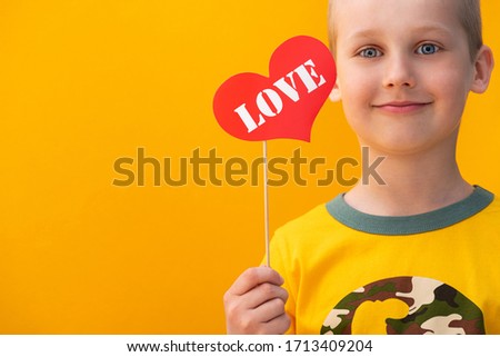 Boy holding a red heart symbol plate with love text on a yellow background