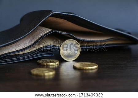Few euro coins of European Union lies on the wooden table next to open empty leather wallet. The topic of reducing the amount of money in the population during the global crisis.