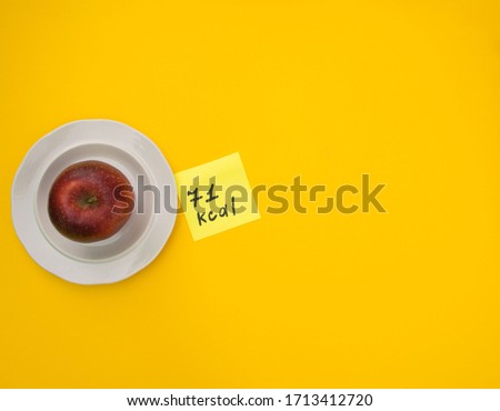 ripe red apple on a yellow background with the number of calories on the sticker. view from above