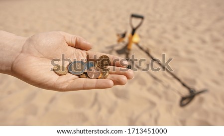 Close up, hands with the coins. Person searching sandy beach with metal detector. Treasure hunt