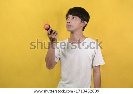 portrait of Asian man wearing a white shirt looking for something with a flashlight isolated on a yellow background
