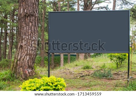 Empty huge billboard sign with copy space at a nature park. White blank mock up with circular steel poles on a road side.
