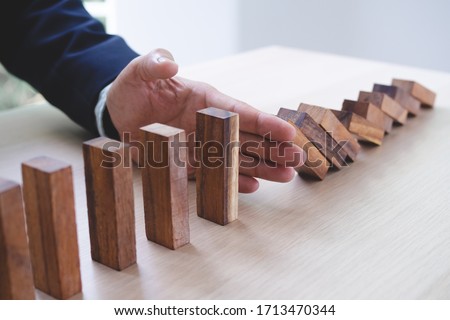 Protection finance from domino effect concept. Hands stop domino effect before destroy stack of money. Royalty-Free Stock Photo #1713470344