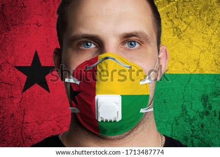 Young man with sore eyes in a medical mask painted in the colors of the national flag of Guinea Bissau. Coronovirus disease  COVID-19 concept.  Man is afraid of getting the flu