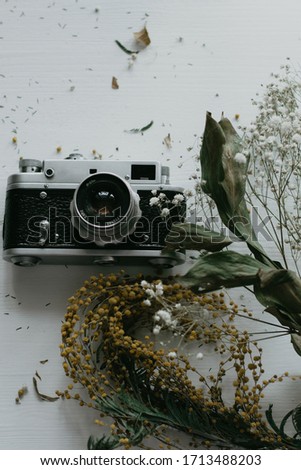 Old camera with white and yellow flowers on a white wooden background