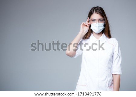 Infectionist doctor in transparent glasses and a medical mask looks into the frame. Protector doctor concept on gray background. Royalty-Free Stock Photo #1713491776