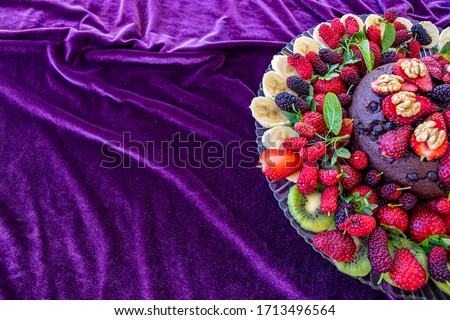 Birthday cake in chocolate with strawberries, blueberries and banana on purple background. Top view. Picture for a menu or a confectionery catalog
