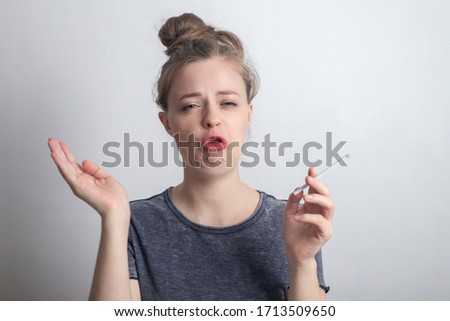 Young caucasian woman girl doesn't like smoking a cigarette, funny disgusted face 