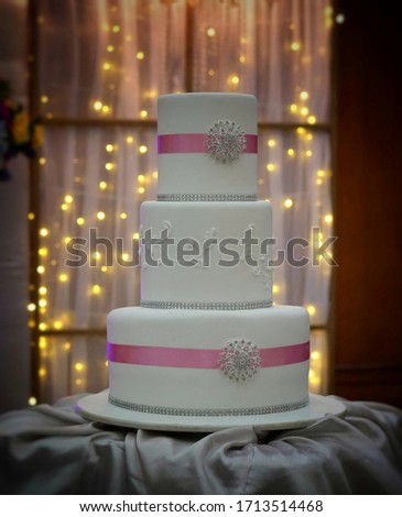 Close up picture of a three-layer white wedding cake with pink accent