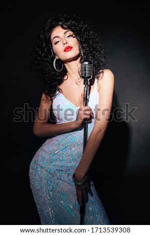 fashion studio photo of beautiful  woman with dark curly hair in elegant dress posing with microphone