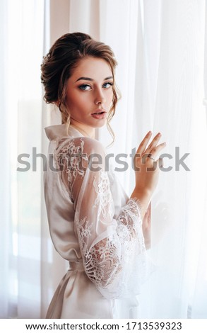 fashion photo of beautiful bride with blond hair in elegant lace robe having morning preparation in wedding day