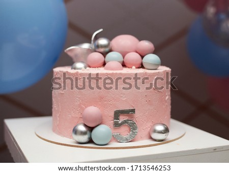 Close-up picture of birthday cake, decorated with pale pink icing and colorful balls. 5 years old celebration party. Family leisure time.