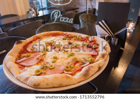 Pizza on the table - in the interior of the pizzeria, next to the menu without text