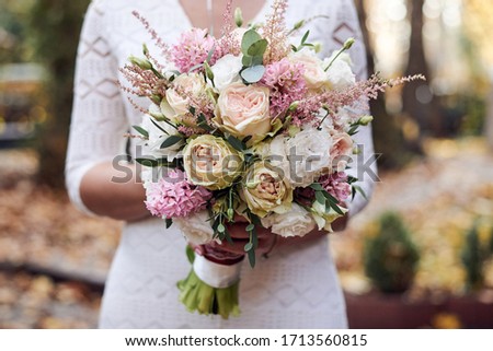 Close-up picture of bride's hands, holding beautiful white and pink flower rose bouquet. Close-up picture of wedding decorations details.