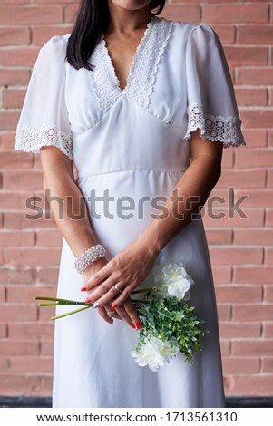 Close-up picture of bride's hands, wearing white tender dress, in front of brick wall in the morning. Wedding day decorations details.