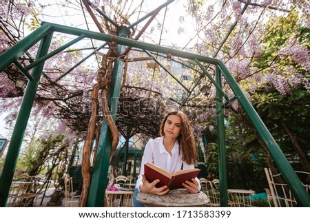 A beautiful young caucasian girl is reading a book in the garden. Spring and flowers
