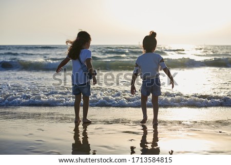 Two small girls sisters, playing jumping on the beach at sunset. Beautiful seaside landscape picture. Family vacation at tropical resort in summer.