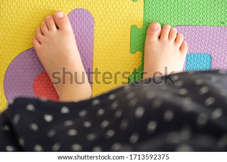 Aerial shot of a girl's feet on a brightly colored floor. She is wearing a polka dot dress. Childhood, innocence, youth, . Soft light in high key