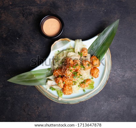 Crispy shrimps salad with shrimps, lettuce, sauce and bamboo leave on a dark background