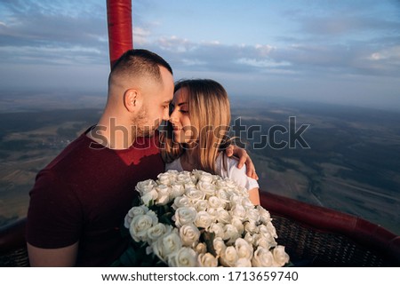 Handsome man with his beautiful girlfriend in air balloon flight. Romantic photo of lovely couple in baloon basket at sunset