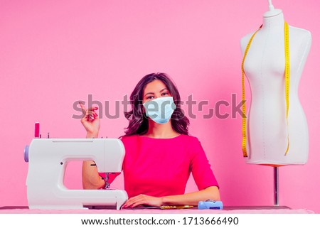 indian woman sews medical eco reusable mask in pink studio background