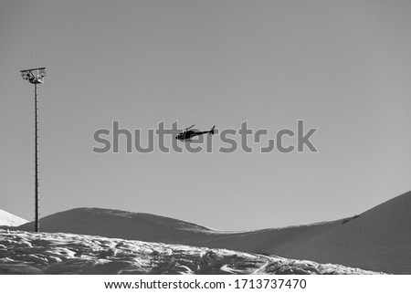 Helicopter in clear sky and snowy ski slope at sunny winter evening. Caucasus Mountains, Georgia, region Gudauri. Black and white toned landscape.

