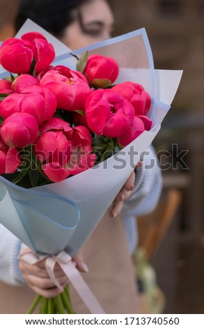 Girl holding bouquet of coral peonies wrapped in blue paper in the blurred background on the street.