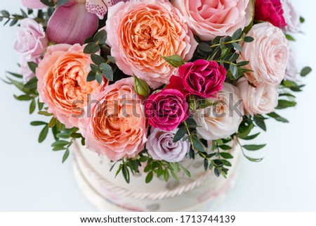 beautiful bouquet in a box on a white table, top view, close-up with blurred background, peony rose, pink rose, purple rose, greens