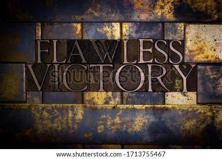 Photo of real authentic typeset letters forming Flawless Victory text on vintage textured grunge copper and gold background