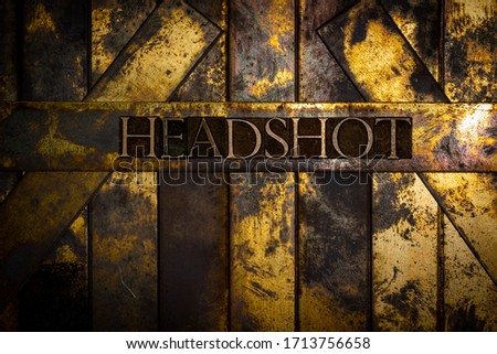 Photo of real authentic typeset letters forming Headshot text on vintage textured grunge copper and gold background