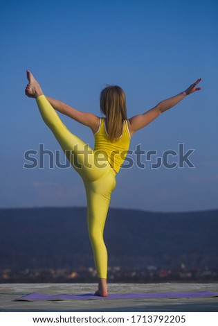 Beautiful blonde girl dancer doing stretching on the roof against the sky and mountains.