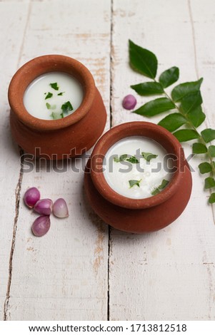 Spiced buttermilk, Chaas or Moru, Sambharam cool refreshing drink for hot summer in a clay pot, Kerala, India. Flavoured Indian buttermilk and ingredients on white wooden background.