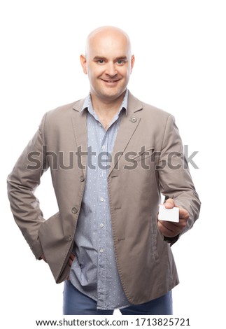 A bald man in a beige suit shows a business card isolated on white.
