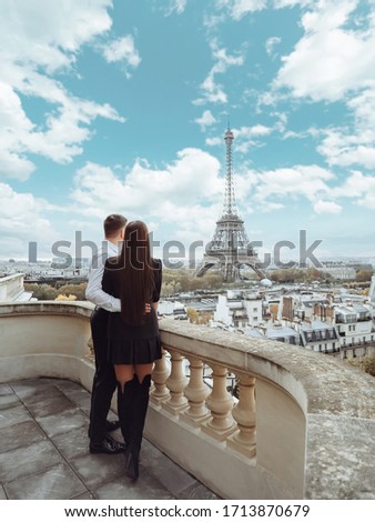 A beautiful young couple is embracing on the balcony of an expensive hotel and looking at the Eiffel Tower in Paris. Eiffel tower on blue sky background