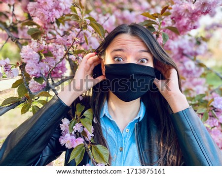a happy girl in sakura taking off protective mask and smelling blooming sakura flowers after coronavirus quarantine