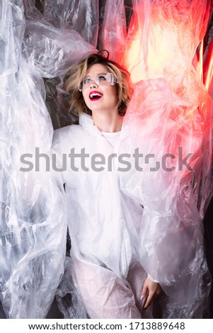 Beautiful model on the background of cellophane with red light, art photography, red lips, the beauty of lipstick. Beautiful scientist woman, world problem of cellophane pollution