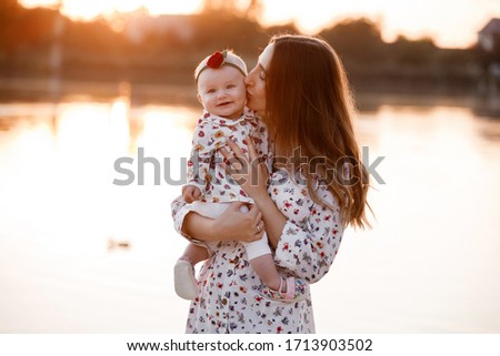 mom kissing her little daughter near the lake on sunset. The concept of summer holiday. Mother's, baby's day. Family spending time together on nature. Family look. selective focus